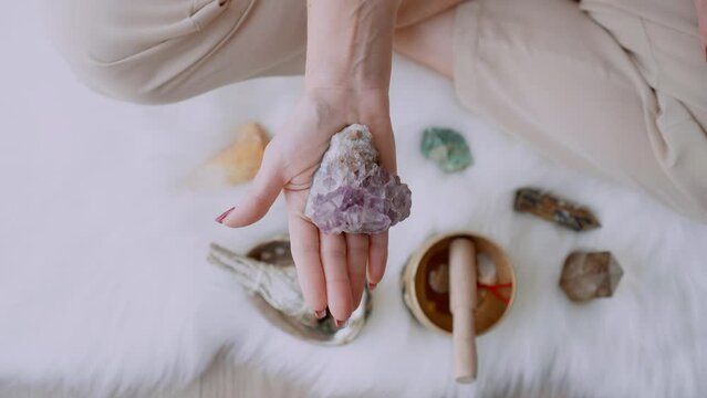 Young caucasian woman holds in the palm of her hand showing an amethyst quartz crystal stone in meditation pose for holistic healing ritual and other elements of abundance and spiritual energy
