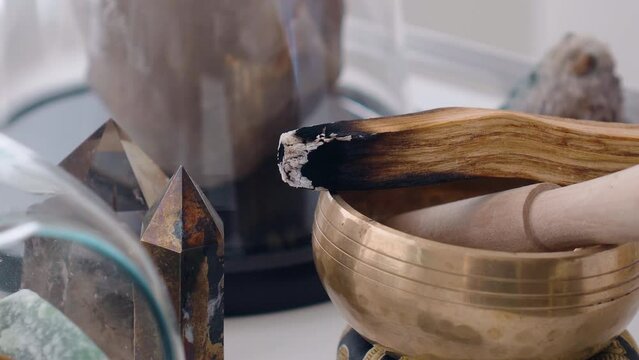 Close up of smoked palo santo lit on a Tibetan bowl to meditate on an altar with quartz for crystal healing holistic ritual