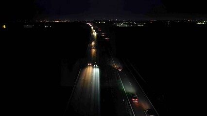 Aerial view of cars driving on a dual carriageway on dark, lights falling on the road, night car traffic.