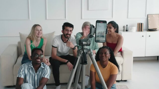 Group of young people taking a selfie or video with phone sitting on the sofa. Smiling multiracial friends students posing for a photo inside in their free time. Bloggers do video blog with monopod