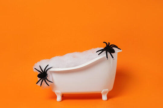 Halloween bathtub filled with spider web and black spiders on bright orange background. Scary concept. Podium for products