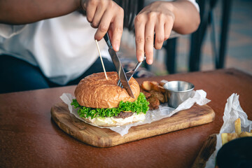 Close-up, a woman in a cafe cuts an appetizing burger.