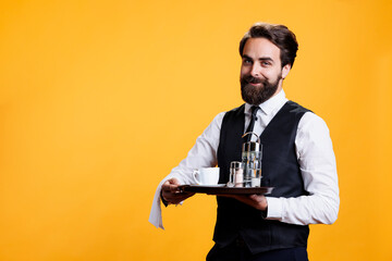 Elegant man butler holding tray to put salt and pepper on table at restaurant, carrying cup of...
