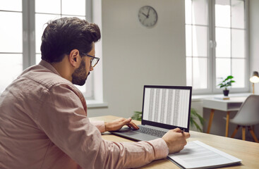 Male bookkeeper sitting at table, making financial report in spreadsheet. Accountant or financial...