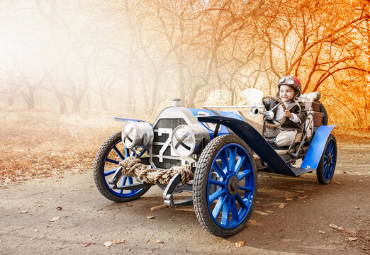 Little boy in the image of a racer finished on an old race car in an autumn park