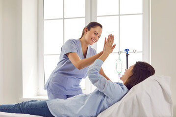 Friendly female gynecologist doctor giving high five to her pregnant woman patient lying on the...