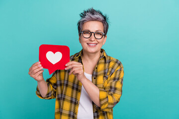 Photo of attractive retired woman hold heart notification dressed stylish checkered yellow clothes isolated on aquamarine color background