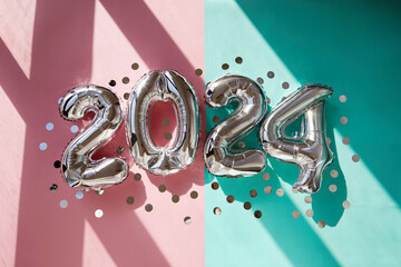 Silver numbers 2024 new year balloons among confetti in sunlight on pink turquoise background Happy...