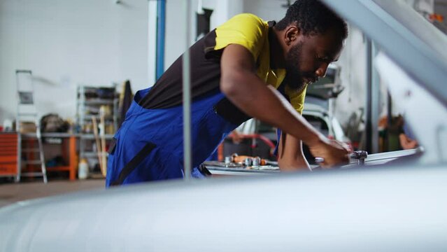 Trained technician in car service picks torque wrench from work station bench, using it to tighten bolts after replacing engine. BIPOC garage worker fixing customer automobile