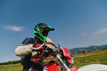 A professional motocross rider, fully geared up with helmet, gloves, and goggles, sitting poised on...