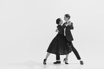 Black and white. Passion and love. Beautiful young woman and man in stylish clothes dancing on white background. Concept of hobby, retro dance, vintage style, choreography, beauty. Monochrome art. Ad