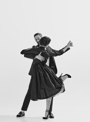 Rhythm and freedom. Black and white. Beautiful young woman in elegant black dress dancing with stylish and handsome man. Concept of hobby, retro dance, vintage style, choreography. Monochrome art. Ad