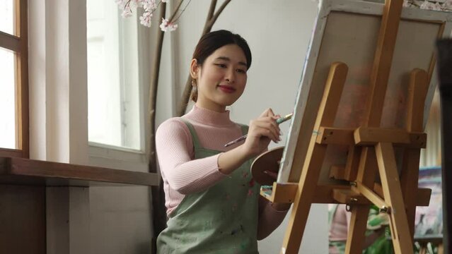 Asian woman artist working on painting with brush and variant acrylic color. Female artist painter on canvas in creative studio as art concept