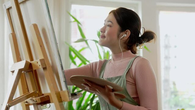 Asian woman artist working on painting with brush and variant acrylic color. Female artist painter on canvas in creative studio as art concept
