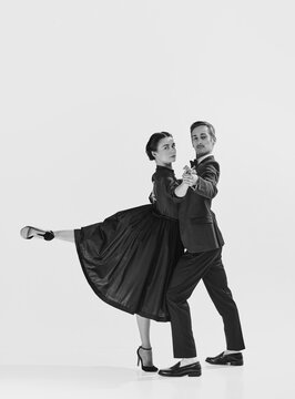 Portrait of beautiful young woman in elegant black dress and handsome man in suit dancing lindy hop. Black and white. Concept of hobby, retro dance, vintage style, choreography. Monochrome art. Ad