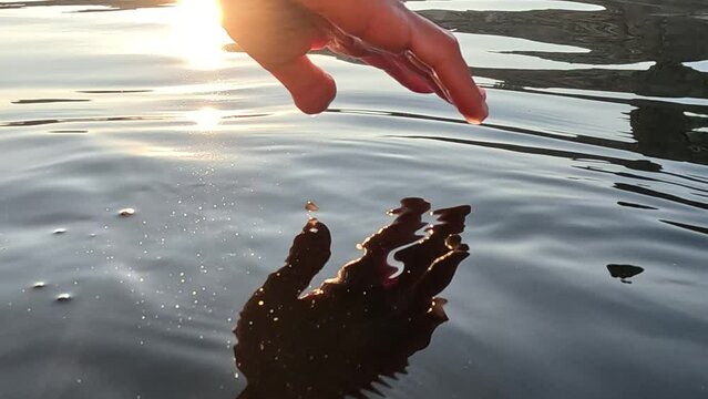 Woman hand sea. Close-up Happy Woman gently caresses water surface at sunset in a warm, golden evening by the sea or lake. Slow-motion Concept of happiness, boat life and holidays in exotic places
