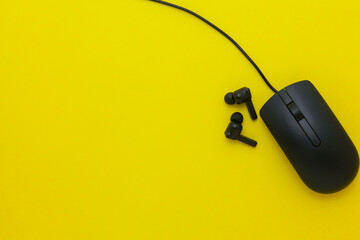 Simple black computer mouse with cord and wireless earbuds isolated on a yellow background, minimal...