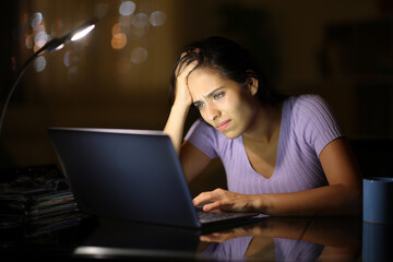 Sad woman in the night at home cheking bad news on laptop