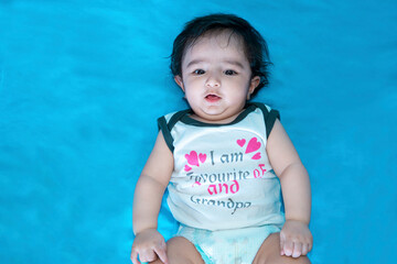 six months old cute indian baby boy wearing diaper lying on floor isolated over blue studio...