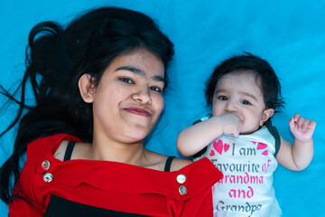 Indian teenager girl lying with six months cute little baby in diaper isolated over blue background. Asian infant child brother and sister, Happy family.