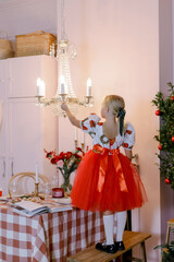 A little girl in the red dress. Christmas holidays at home. A kitchen and a  lamp in room the pink color interior.