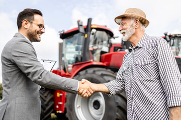 Successful tractor sale. Farmer and dealer shaking hands after purchase of agricultural machines.
