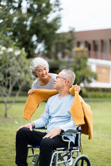 Happy Life Retirement, Asian Elderly wife take care husband sitting on wheelchair with warm cloth in the park relaxing with love, Senior couple take care of each other.