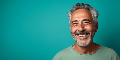 Studio portrait of smiling and friendly middle aged man with gray hair and beard, colorful aqua blue t shirt and background