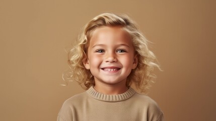In this heartwarming portrait, a little boy with golden locks beams brightly against a soft beige backdrop.