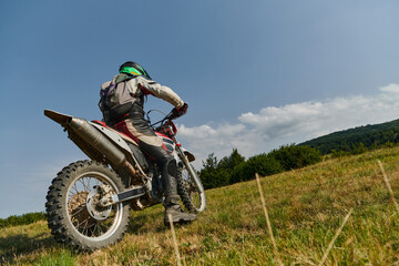 A motorcyclist equipped with professional gear, rides motocross on perilous meadows, training for...