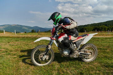 A motorcyclist equipped with professional gear, rides motocross on perilous meadows, training for...