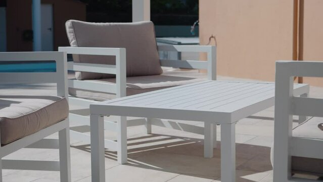 Slow orbiting shot of garden patio furniture with a swimming pool behind