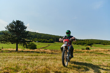 A motorcyclist equipped with professional gear, rides motocross on perilous meadows, training for...