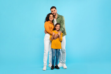 Healthy family relationship. European dad and mom embracing daughter, posing over blue background,...