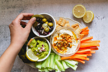 Person dipping carrot stick into hummus decorated with vegetables