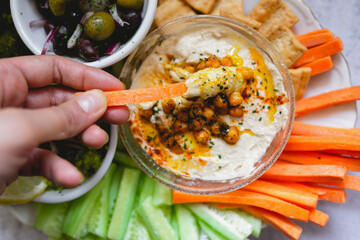 Person dipping carrot stick into hummus decorated with vegetables
