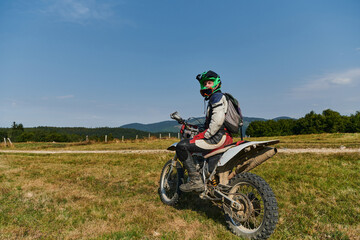 A motorcyclist equipped with professional gear, rides motocross on perilous meadows, training for...