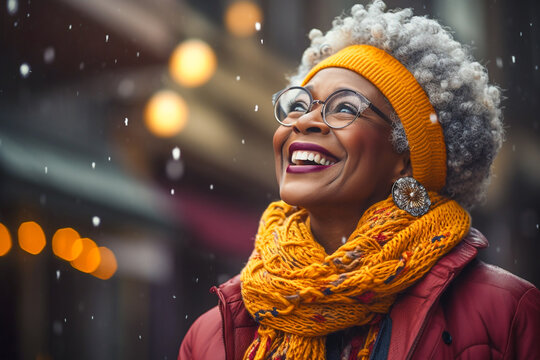 portrait of happy mature black woman with white hair looking up snowing in winter with scarf