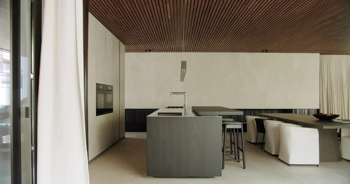 Room with kitchen island, bar stools, sink with faucet, household integrated appliances and dining table with chairs at cottage house with modern interior.