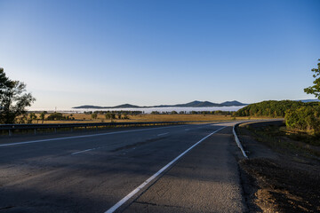 Asphalt road in the mountains with blue sky and white fog