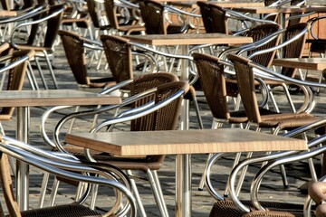 Wooden tables with metal pedestals, chairs with wicker backs and metal armrests and legs in outdoors