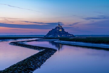 Sunrise view of the historic Mont Saint Michel castle in France, illuminated by a vibrant purple sky