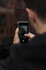 Man capturing a photo of a tall, modern building with his smartphone