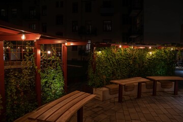 Row of wooden benches arranged in a circle in the dark with lights behind them.