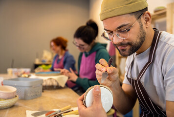 Group of people working in pottery studio workshp making bowl from clay.