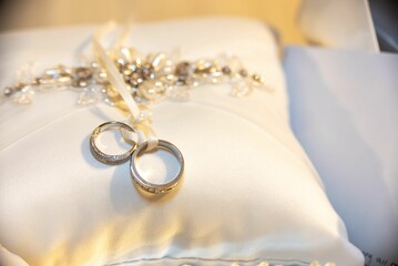 Close-up shot of two gold wedding rings resting on a white pillow with a soft focus background