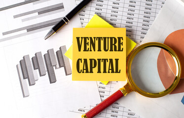 VENTURE CAPITAL text on a sticky on the graph background with pen and magnifier