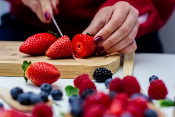 Female slicing strawberries with a kitchen knife in front of fresh strawberries
