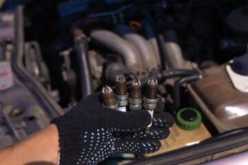 Close-up of a hand in a black glove with four used car candles on the background of the engine. Concept of car repair