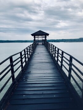 Wooden pier with e shelter on the water surrounded by green trees on a gloomy day © Anulqa/Wirestock Creators